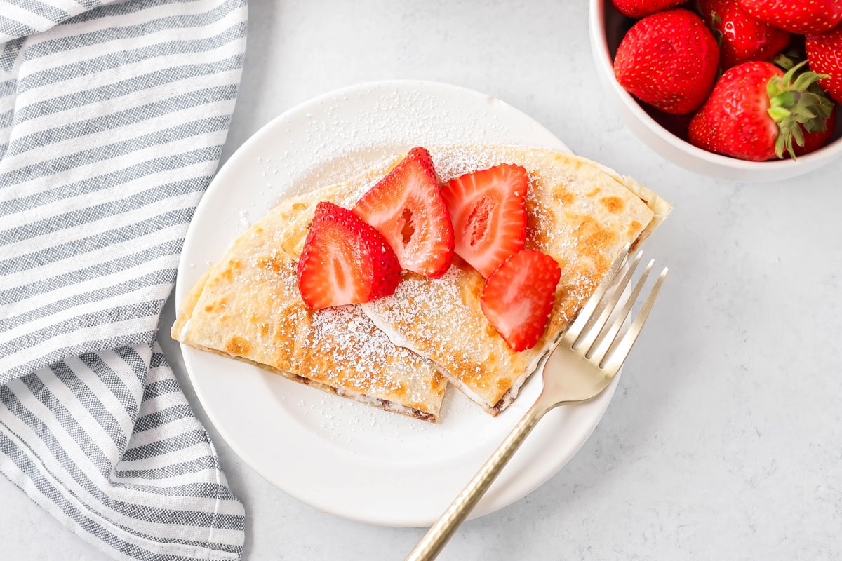 Dessert quesadillas on white plate with sliced strawberries on top.