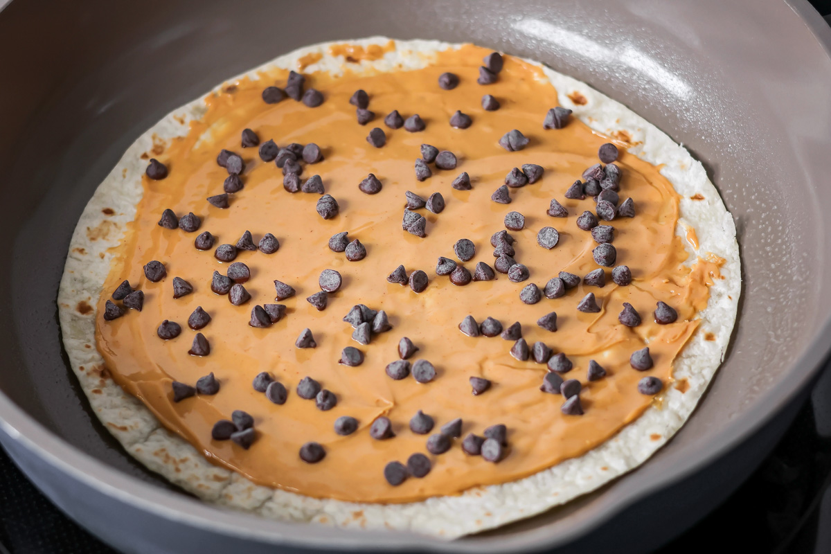 Tortilla with peanut butter and mini chocolate chip cooking in skillet.
