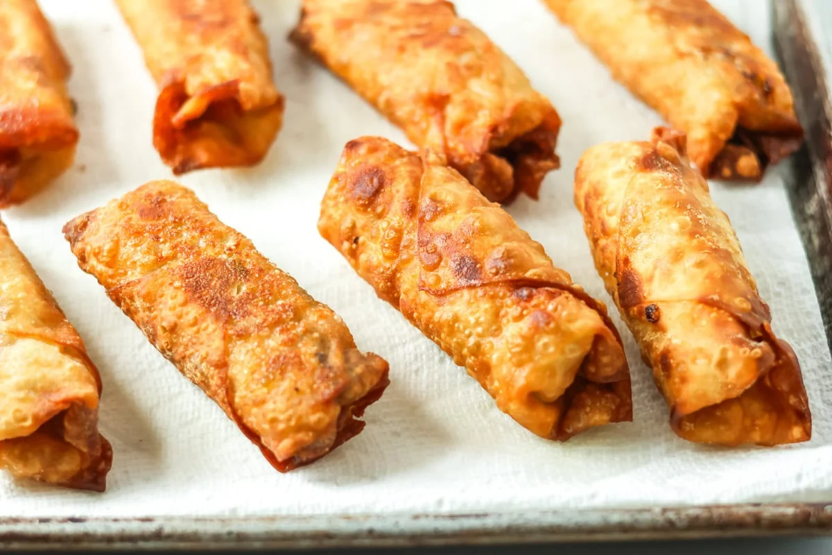 Eight golden eggs rolls on a paper towel lined pan.