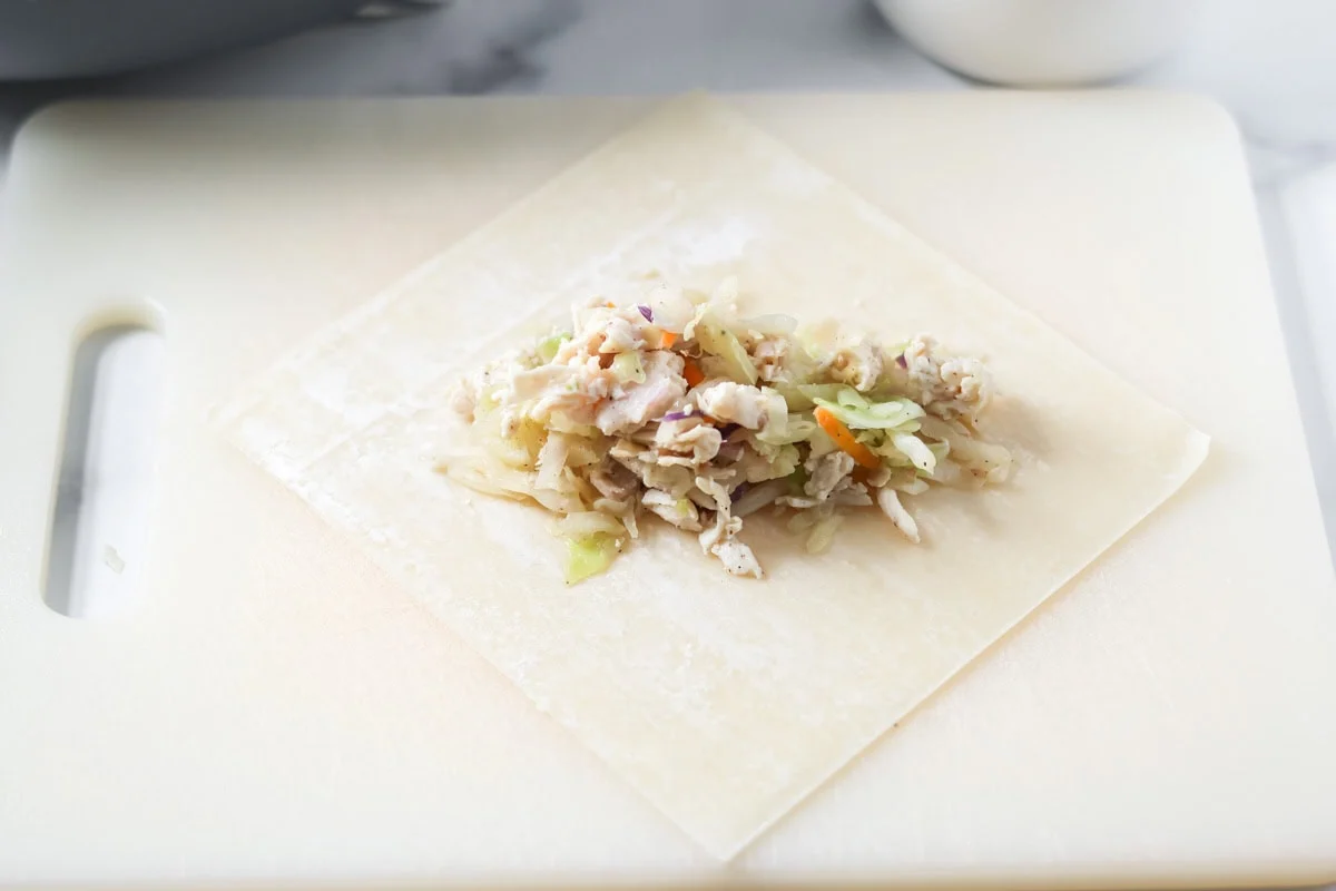 An egg roll wrapper on a cutting board with filling down the center.