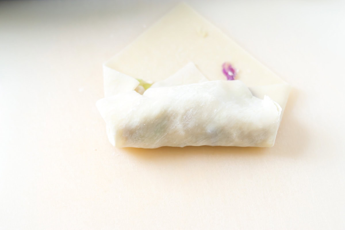 The bottom corner of the egg roll folded up over the filling.