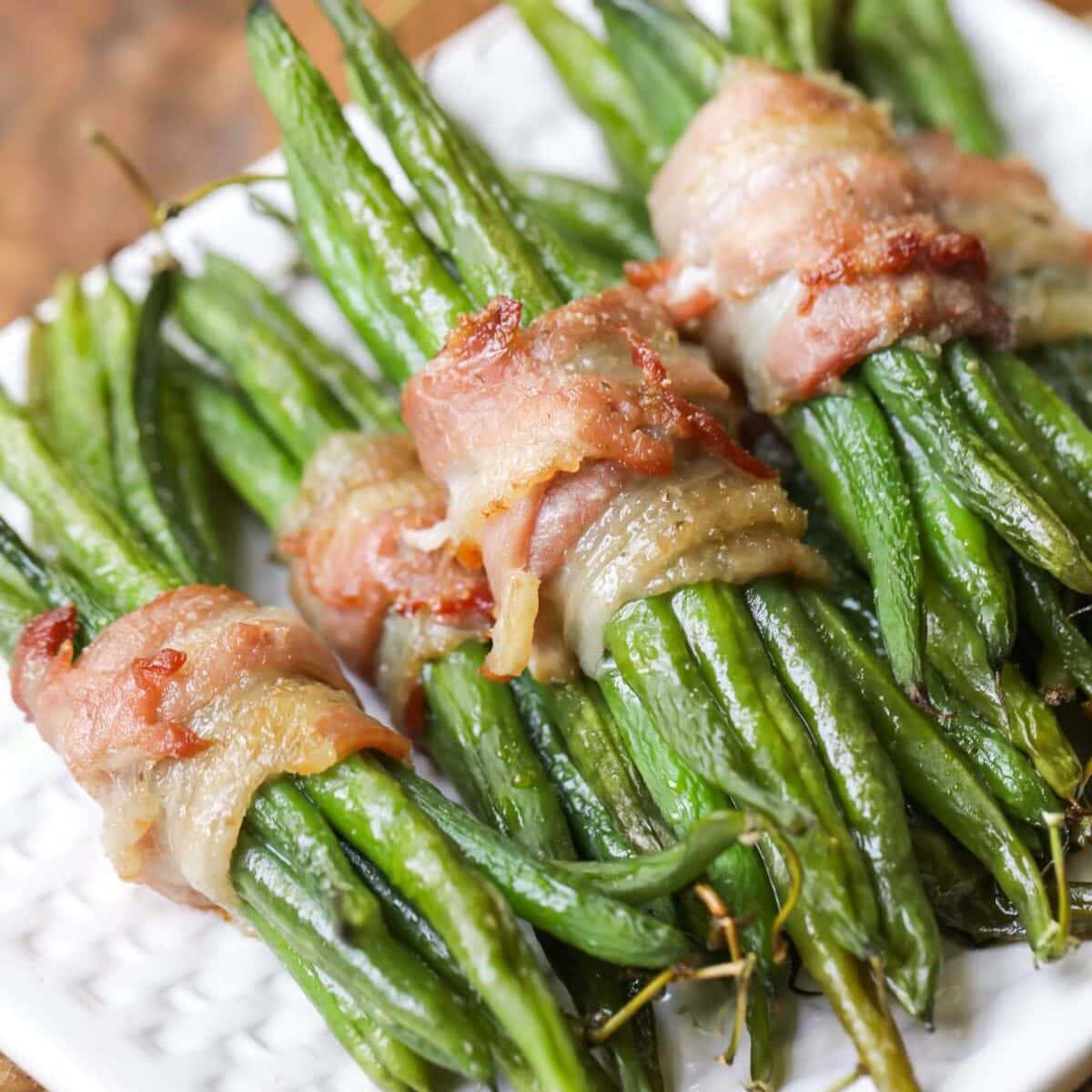 Green bean bundles wrapped in bacon stacked on a white plate.