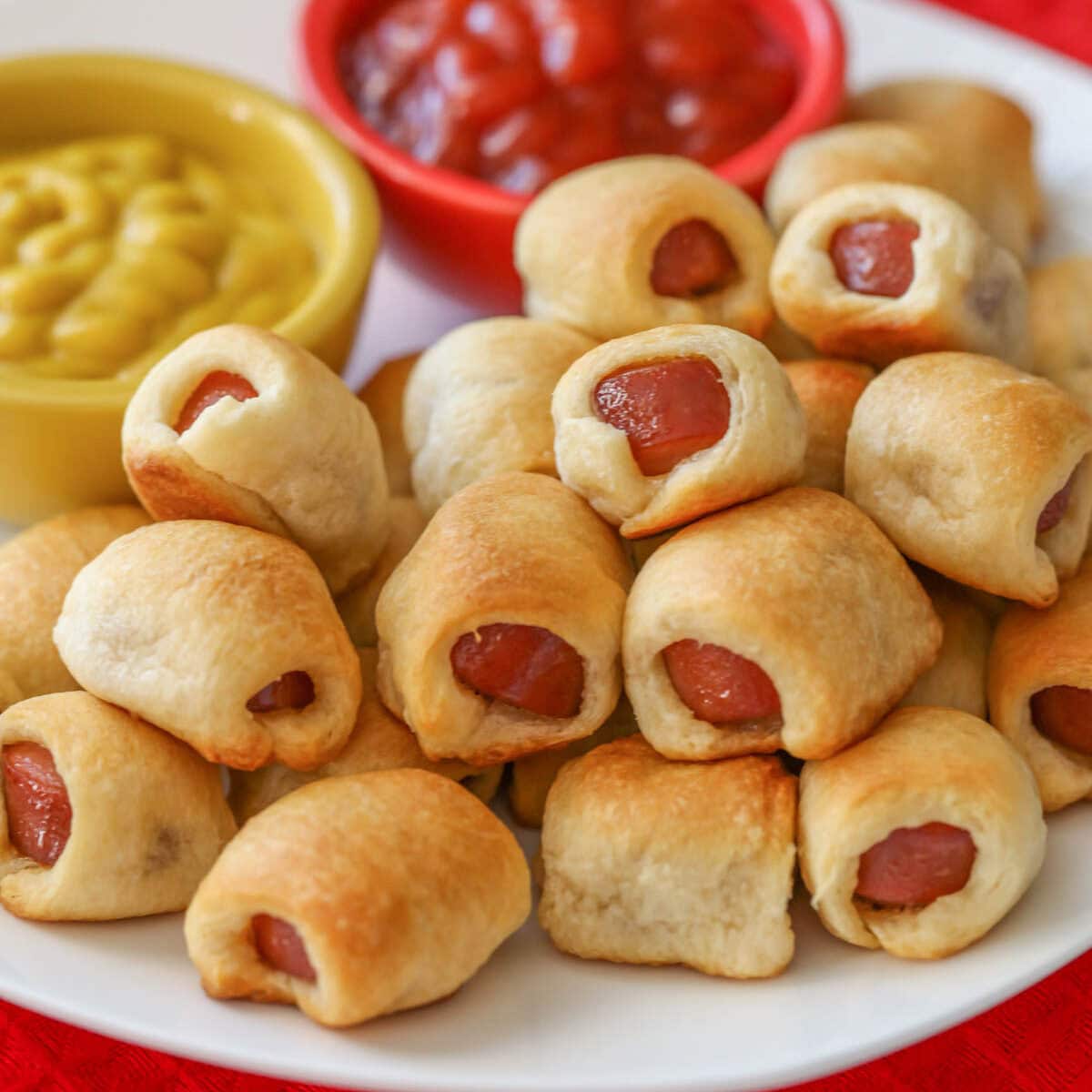 Mini hot dogs stacked on top of each other on white plate.