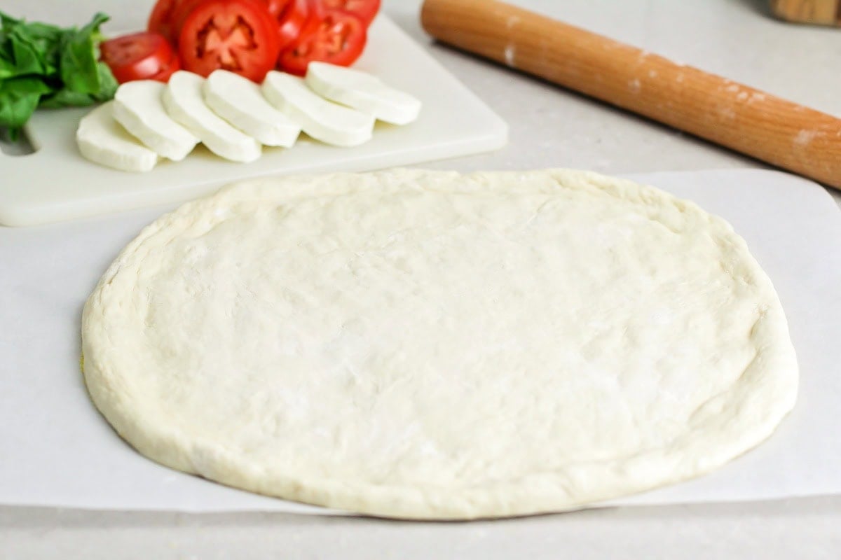 Margherita pizza stars fresh basil, mozzarella cheese, and the best ripe tomatoes. It's simple, delicious, and light. Rolled out pizza dough on a piece of parchment paper.