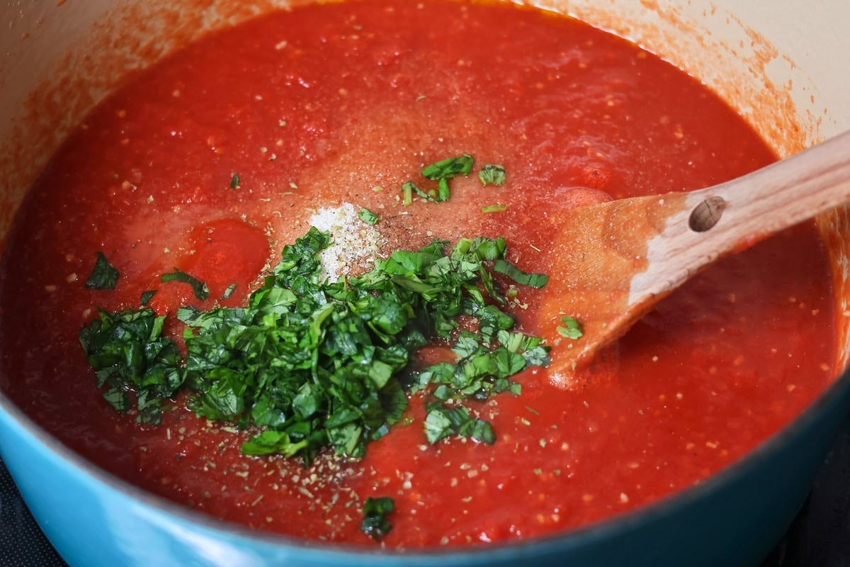 This simple homemade marinara sauce simmers fresh tomatoes with fragrant herbs and garlic for a versatile flavor explosion. Mixing seasonings into red sauce in a pot.