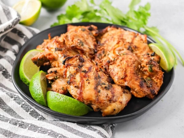 Mexican chicken marinade recipe with chicken on black plate with limes and cilantro.