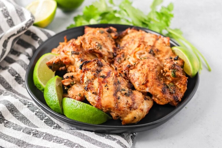 Mexican chicken marinade recipe with chicken on black plate with limes and cilantro.