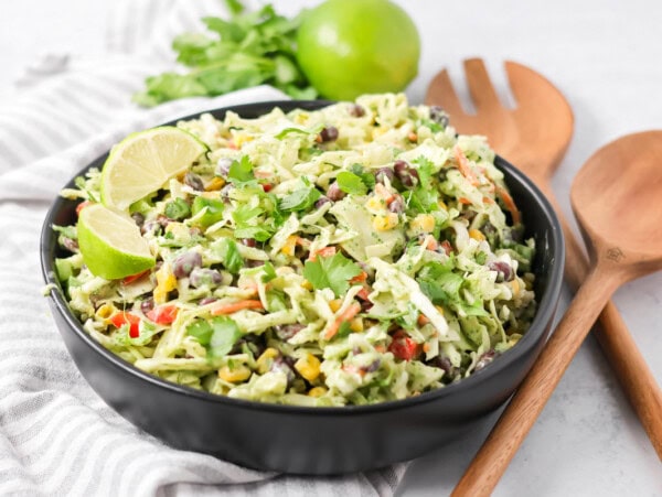 Mexican coleslaw recipe in black bowl with ingredients on the side.
