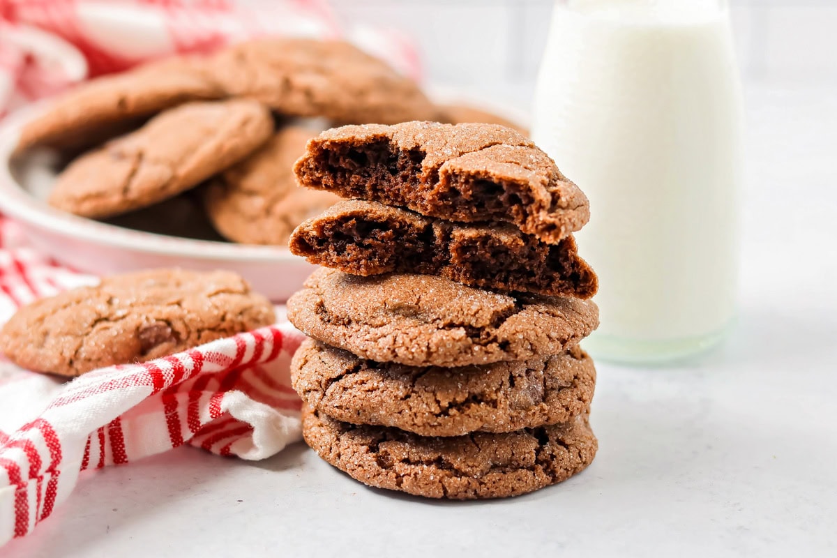 Easy Mexican hot chocolate cookies are soft and chocolatey with cinnamon sugar sparkle and a hint of heat, and perfect for sharing. Five stacked cookies in front of a pate of cookies with a bottle of milk.