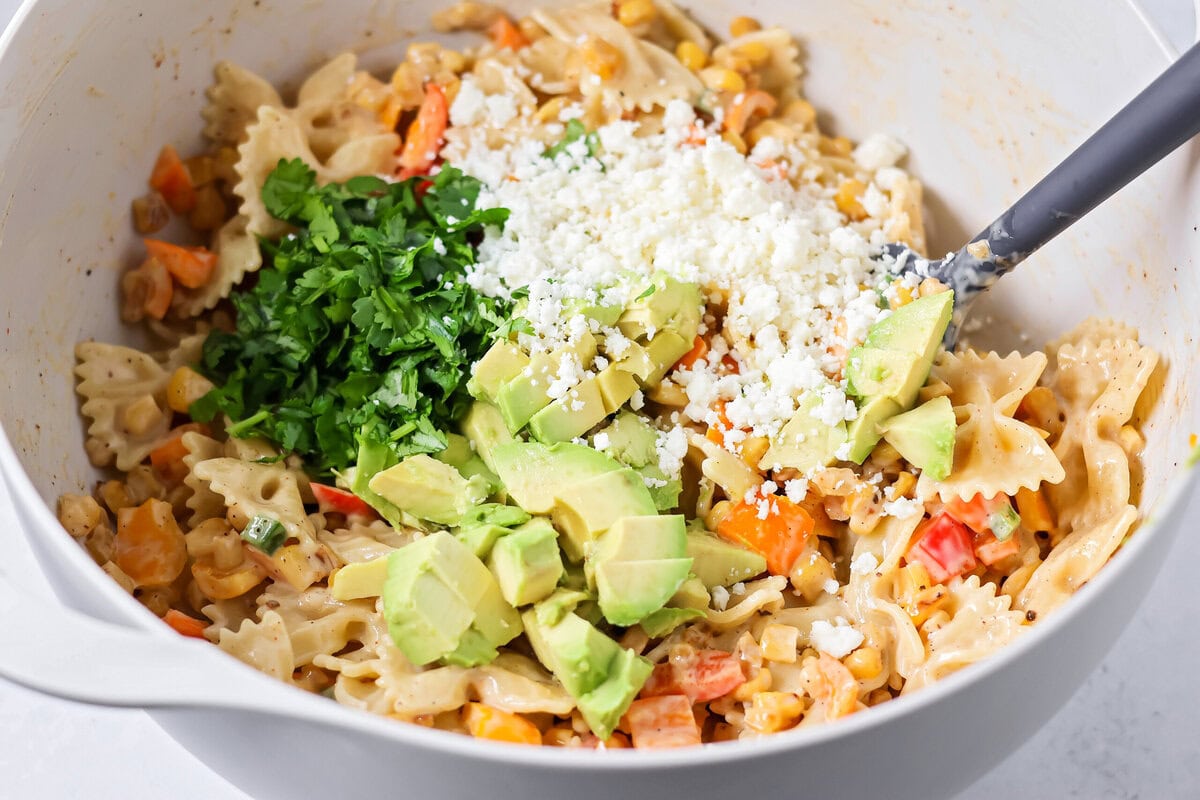 Creamy Mexican street corn pasta salad is a perfect balance of flavor, quick to toss together, and perfect for parties and easy dinners. Topping pasta salad with avocado, cheese, and cilantro.