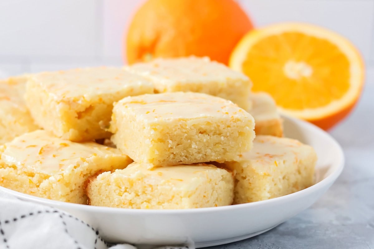 Soft orange brownies are made with simple ingredients, a quick bake, and a bright flavor that makes every slice feel special. A stack of cut orange brownies on a serving plate.