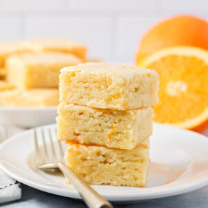 A stack of 3 orange brownies on a plate.