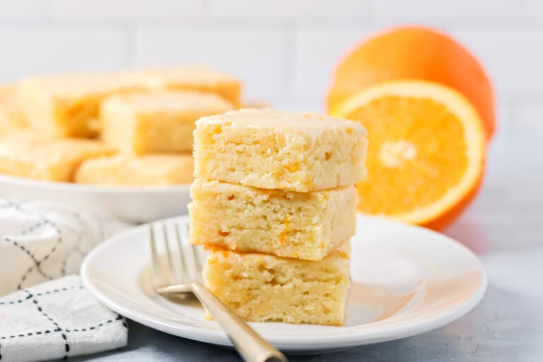 A stack of 3 orange brownies on a plate.