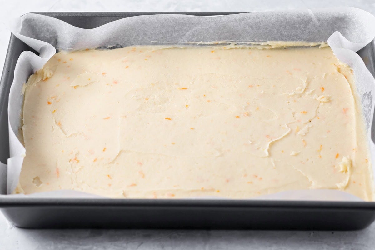 Soft orange brownies are made with simple ingredients, a quick bake, and a bright flavor that makes every slice feel special. Orange brownie batter in a parchment lined baking pan.