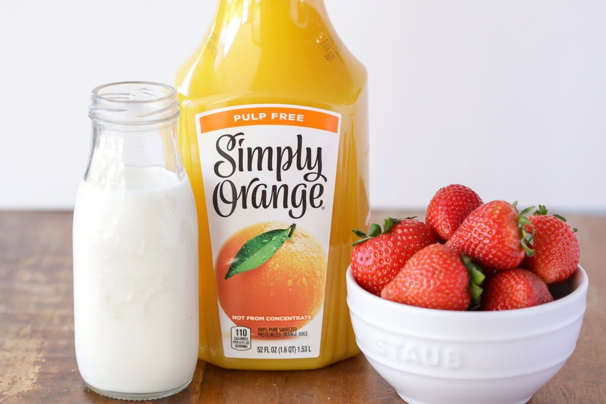 Blend a bright orange juice smoothie in 5 minutes, packed with strawberries, vanilla, and vitamin C for a quick breakfast the kids love. Ingredients to make an orange juice smoothie on a kitchen counter.