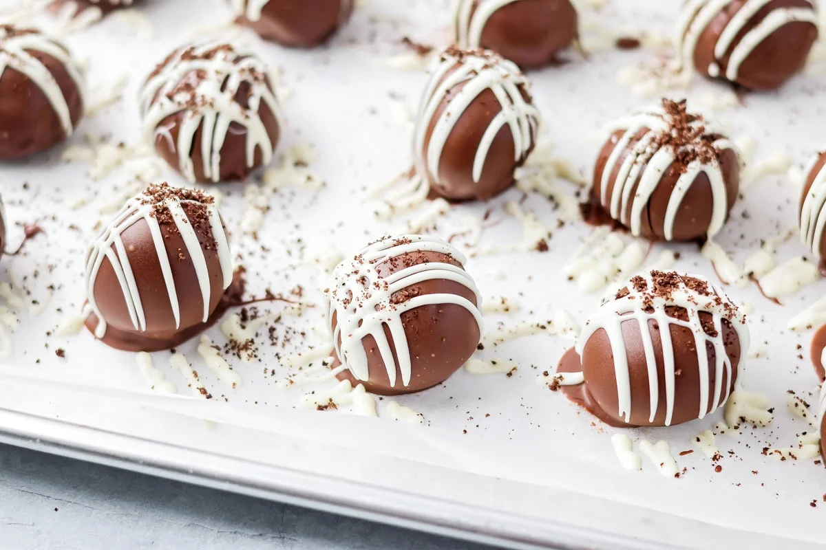 No-bake Oreo cream cheese balls are a three ingredient treat with a silky center and chocolate coating, ideal for every occasion. Chocolate dipped Oreo balls topped with a white drizzle pattern and Oreo cookie crumbs.