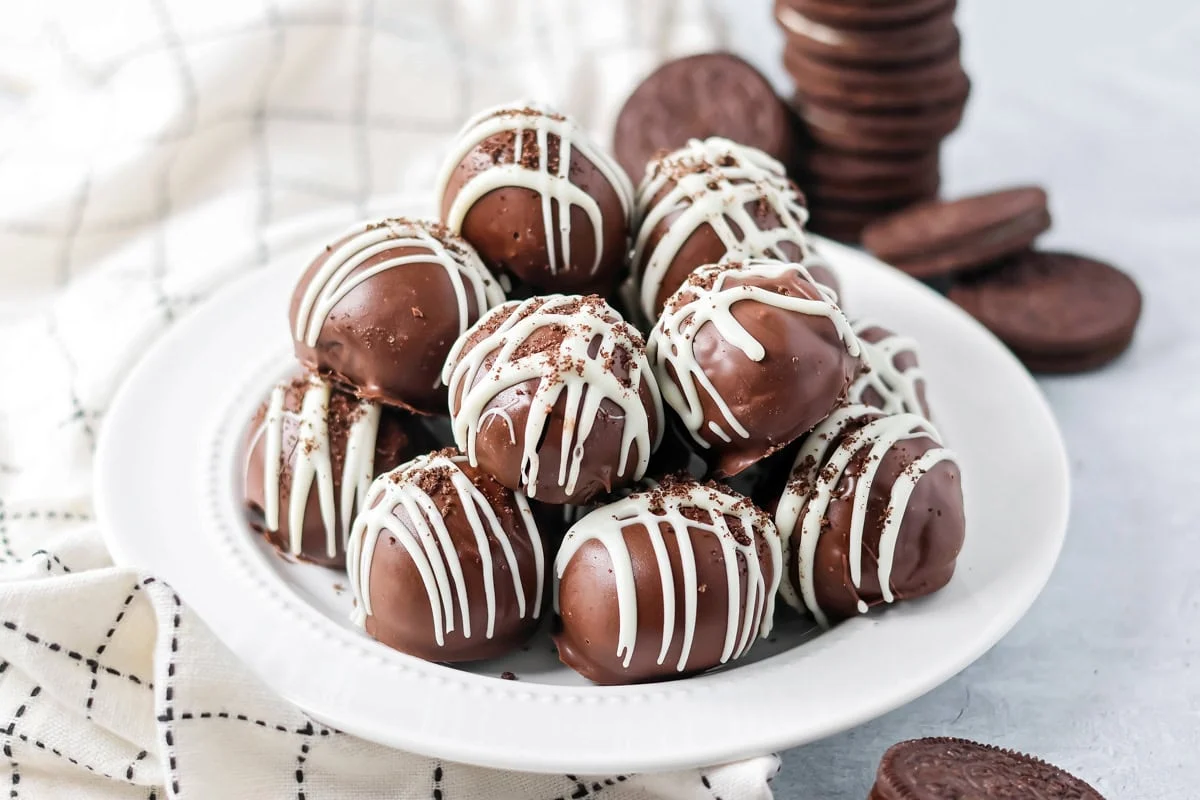 No-bake Oreo cream cheese balls are a three ingredient treat with a silky center and chocolate coating, ideal for every occasion. A serving plate full of stacked Oreo truffle balls.
