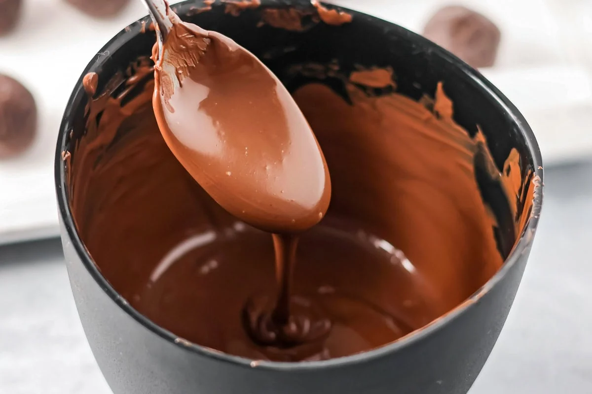 No-bake Oreo cream cheese balls are a three ingredient treat with a silky center and chocolate coating, ideal for every occasion. Drizzling melted chocolate off a spoon into a bowl of chocolate.