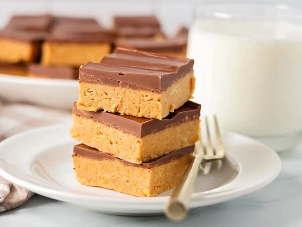 Peanut butter bars stacked on top of each other on white plate.
