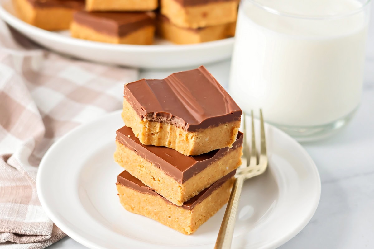 Peanut butter bars stacked on top of each other on white plate with bite taken out.