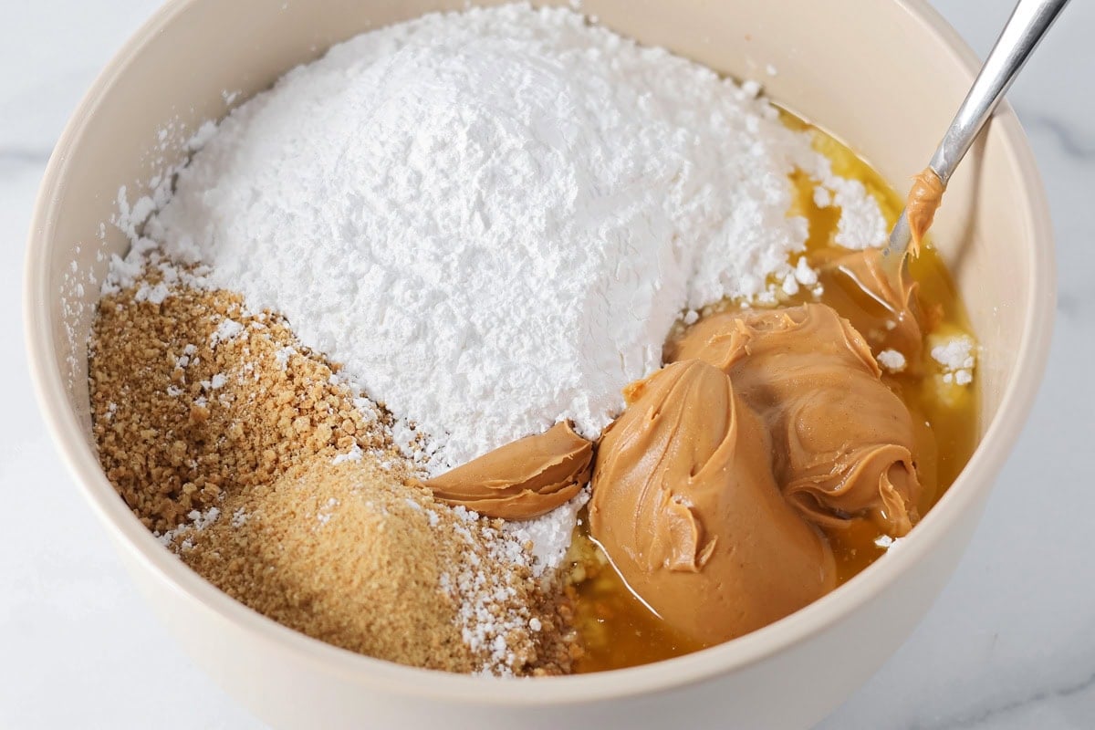 Graham cracker crumbs, powdered sugar, butter and peanut butter being mixed in a bowl.
