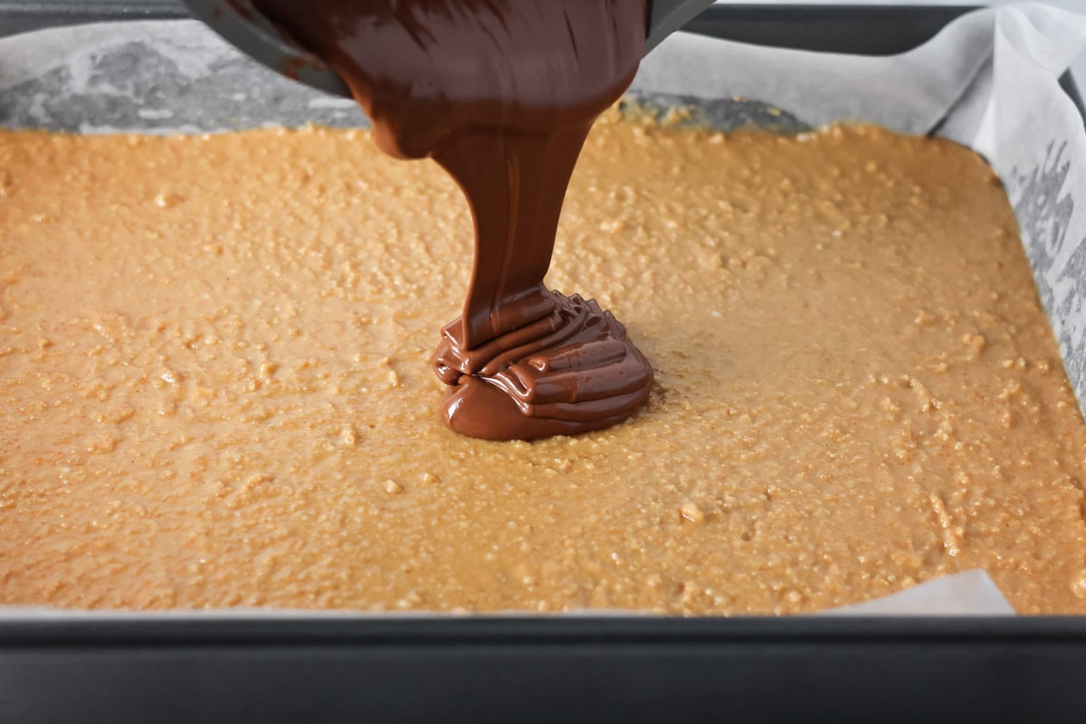 Chocolate topping for peanut butter bars recipe being poured over 9x13.