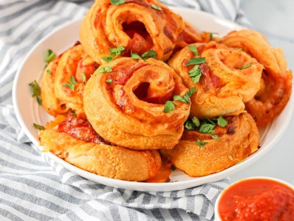 Pizza pinwheels stacked on white plate sprinkled with parsley.