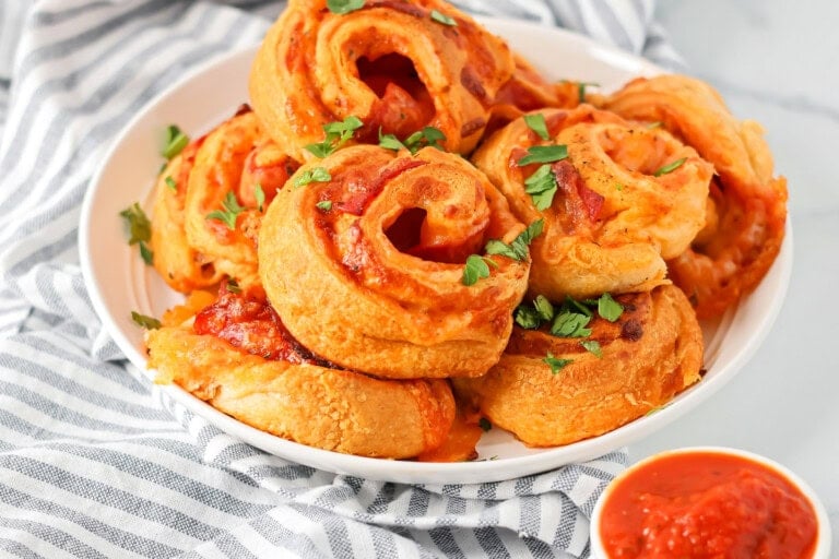 Pizza pinwheels stacked on white plate sprinkled with parsley.