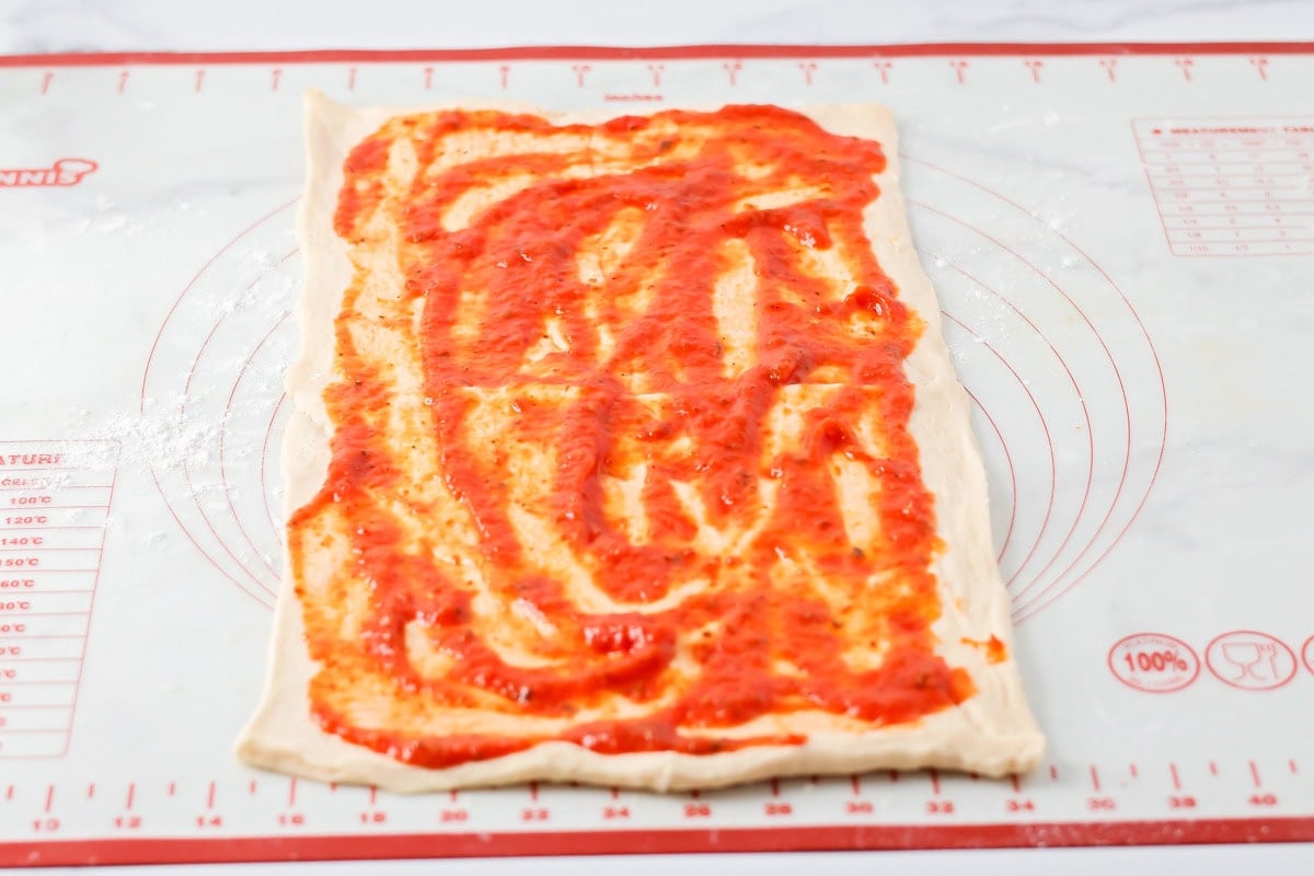 Pizza sauce being added to crescent dough.