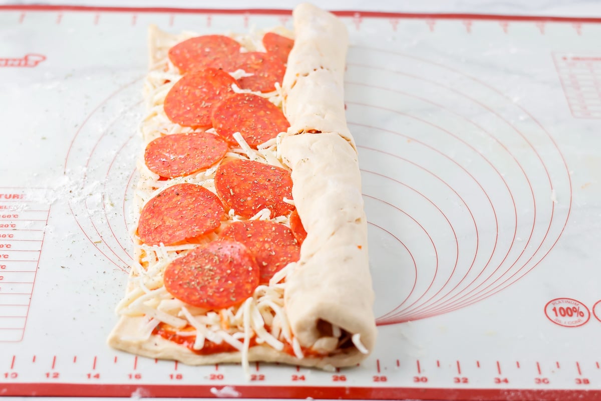 Crescent dough being rolled up with pizza ingredients added to the middle.