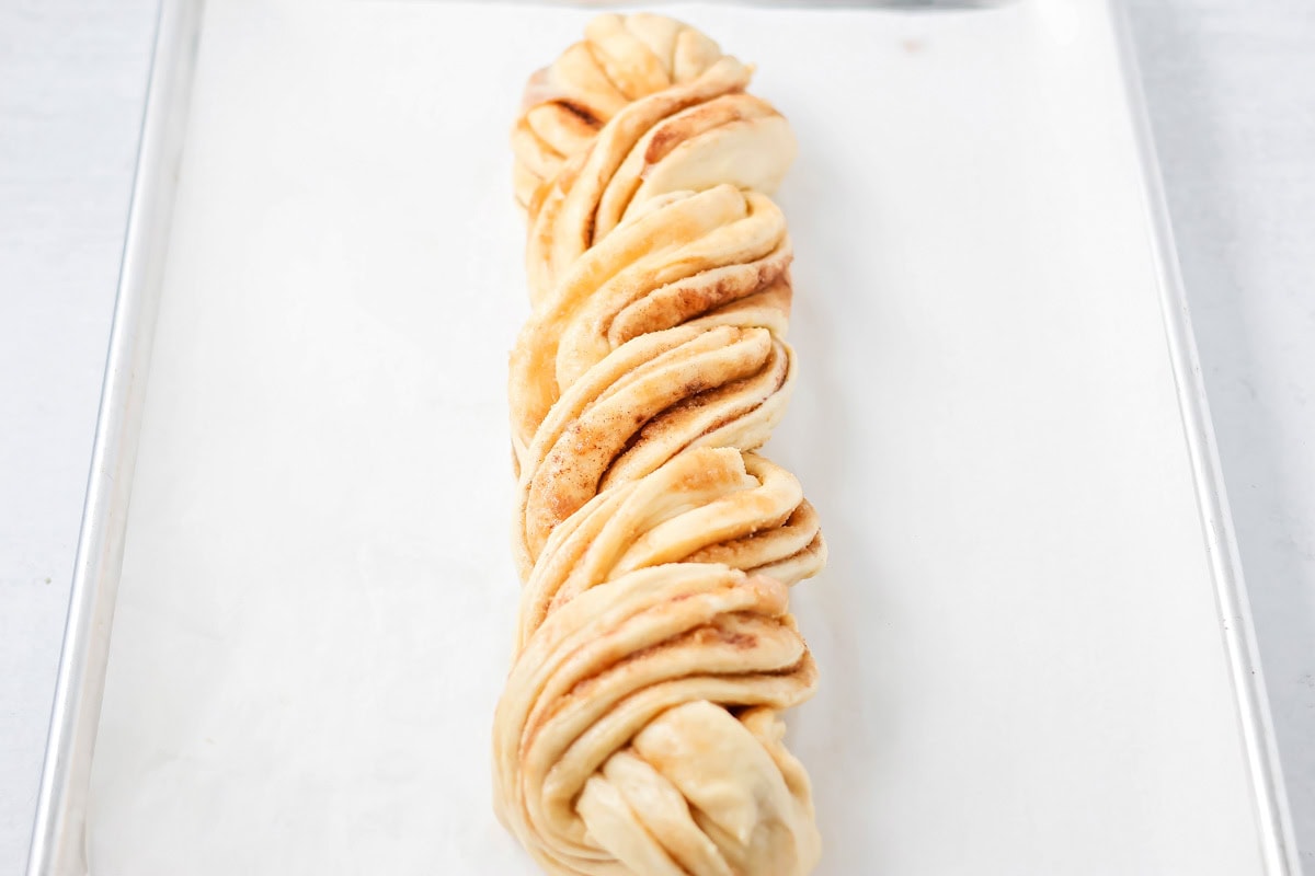 Quick cinnamon twists are made with a simple soft, buttery dough, and swirled with cinnamon sugar and are perfect for breakfast or dessert. Twisted log of dough on a baking sheet.