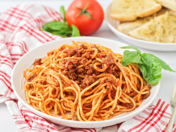 Easy spaghetti recipe dished on white plate with basil on the side.
