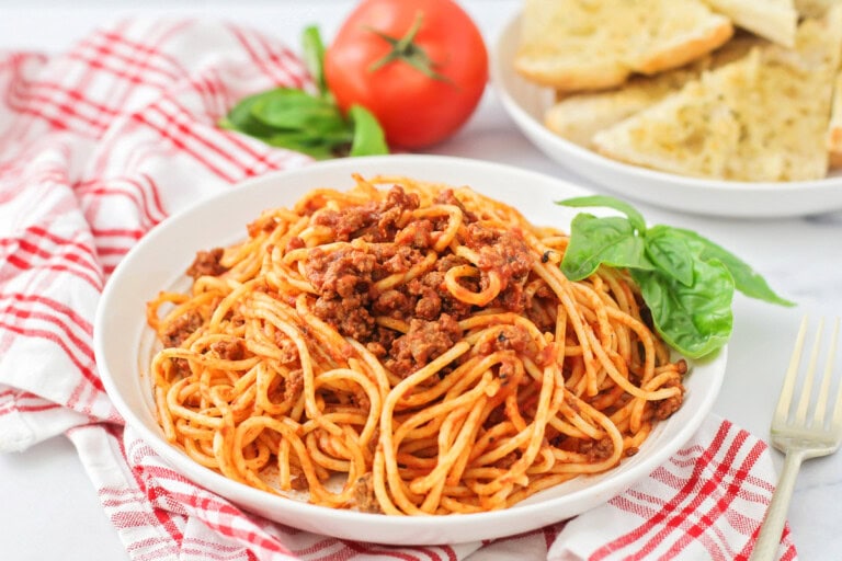 Easy spaghetti recipe dished on white plate with basil on the side.