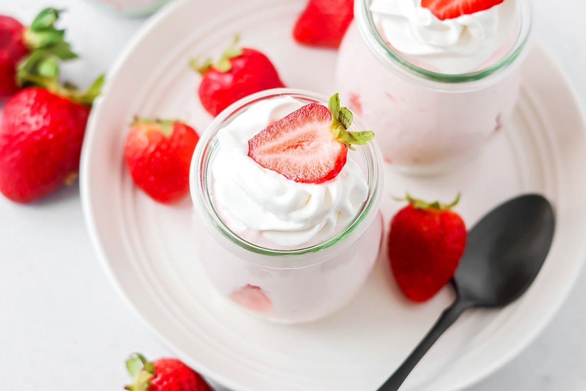 Close up image of strawberry mousse in glass jar with strawberry on top.