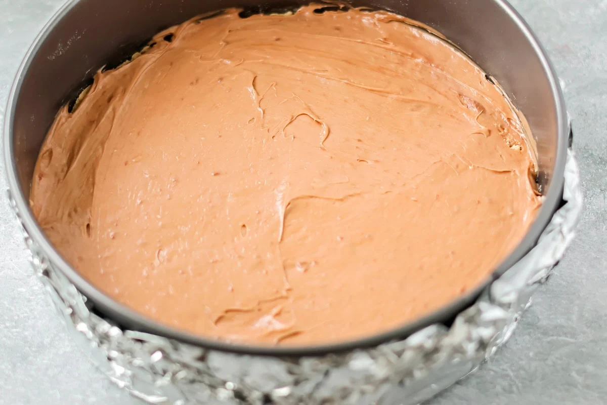 Chocolate cheesecake filling spread in a springform pan.