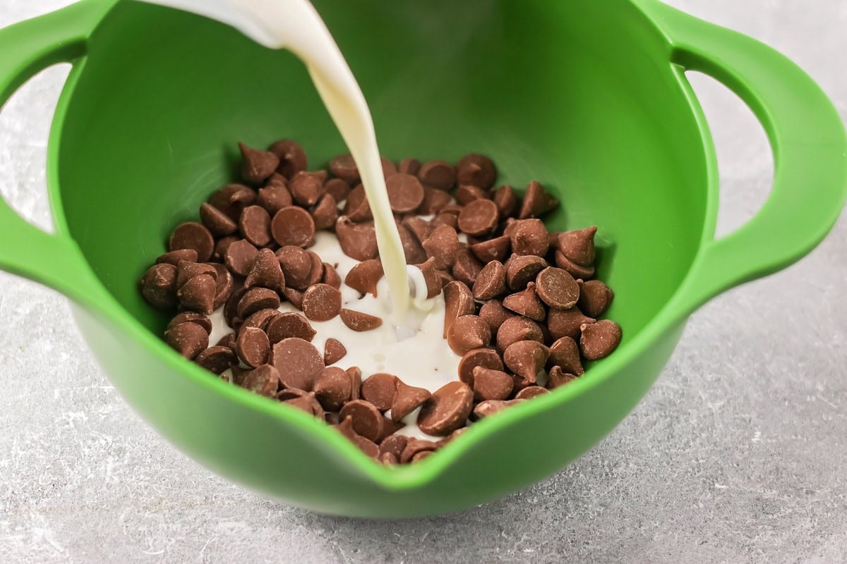 Pouring heavy cream over chocolate chips in a mixing bowl.