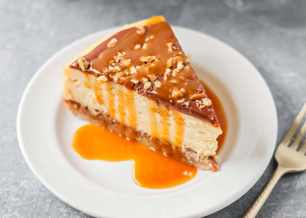 A slice of turtle cheesecake on a serving plate with a caramel sauce drizzle over it.