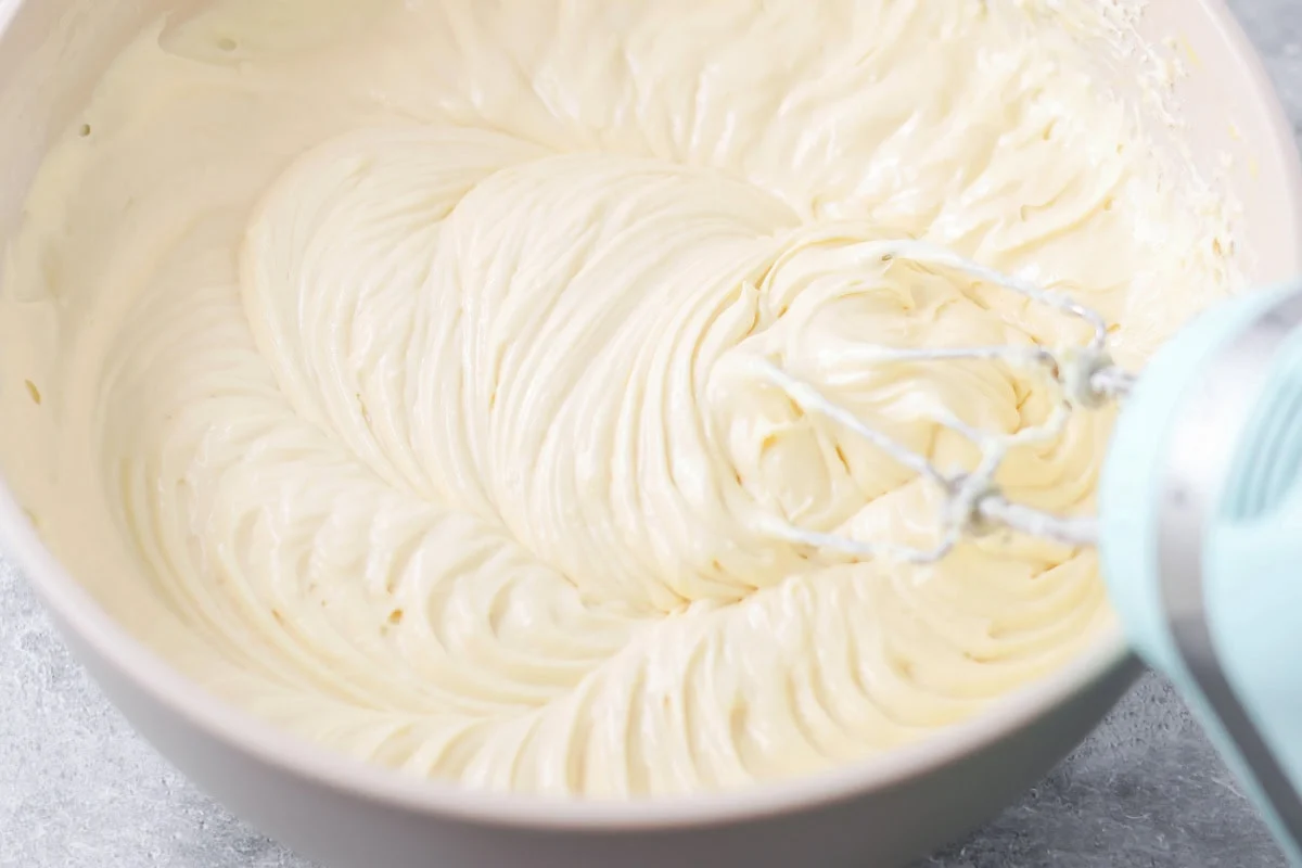 Mixing cheesecake filling in a bowl with an electric mixer.