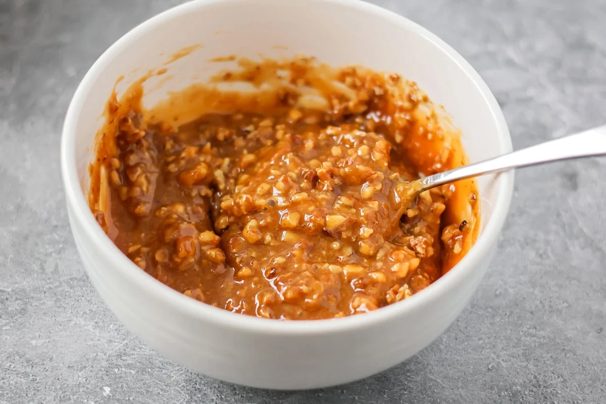 Mixed caramel sauce with chopped pecans in a bowl.