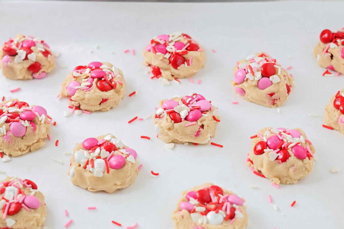 Valentines Day cookies are soft and chewy with chocolate pops of pink, red, and white M&M's. They are Valentine's perfection! Cookie dough balls topped with M&Ms and sprinkles.