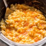 Crockpot cheesy potatoes close up image being scooped out of slow cooker.