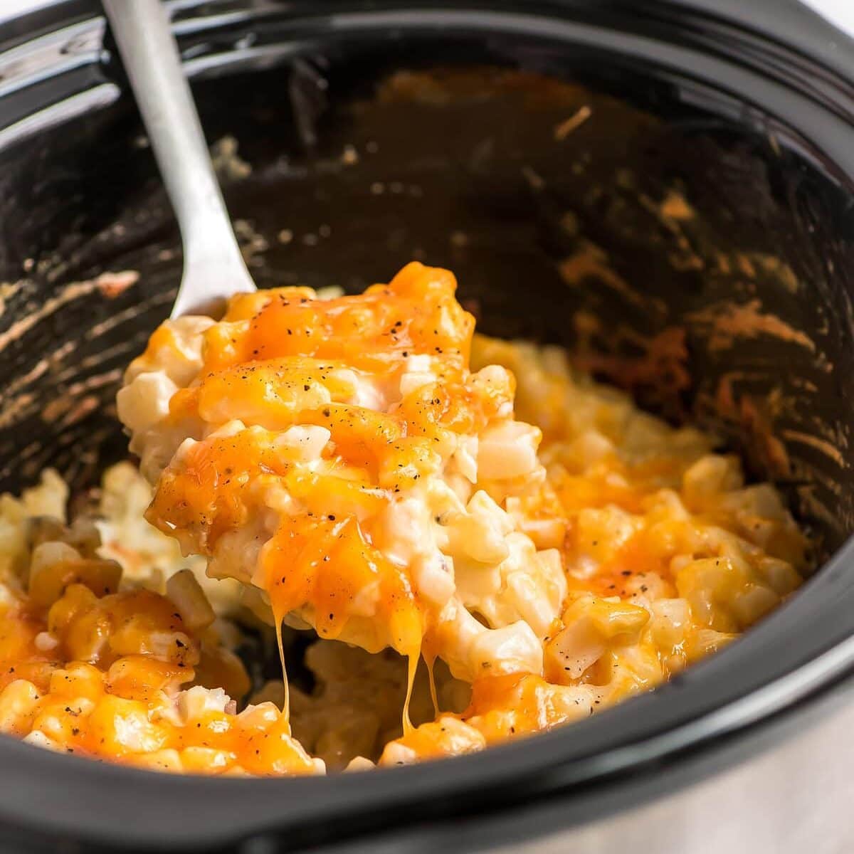 Crockpot cheesy potatoes being scooped out of the slow cooker.