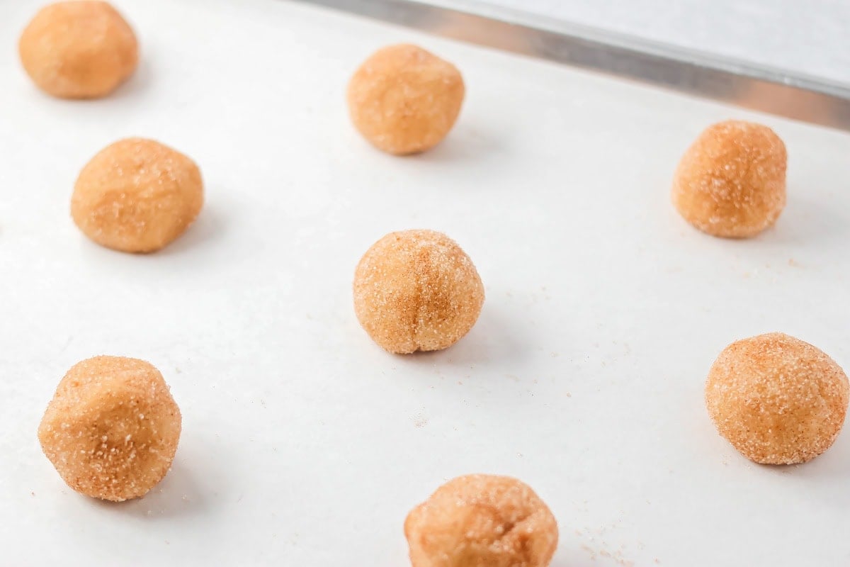 Family favorite brown butter snickerdoodle recipe is easy to make with a soft center, classic tang, and cozy flavor. Coated cookie dough balls on a baking sheet.