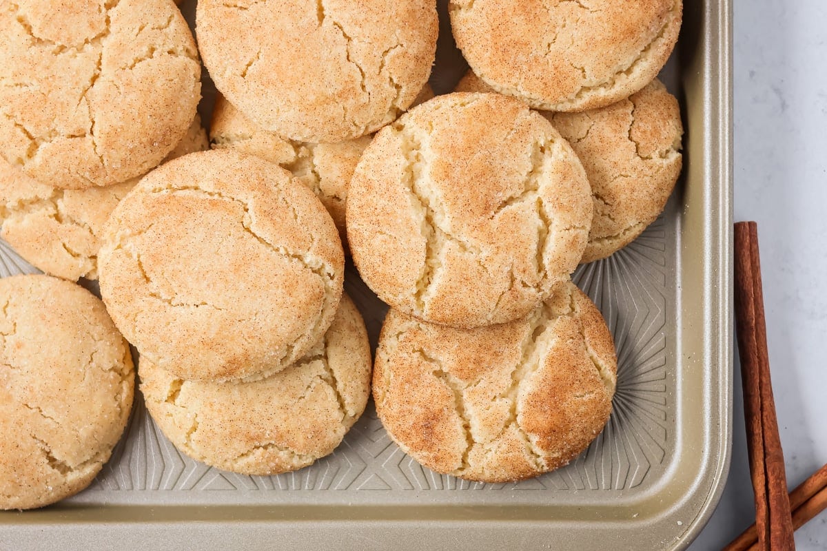 Family favorite brown butter snickerdoodle recipe is easy to make with a soft center, classic tang, and cozy flavor. Brown butter snickerdoodles stacked on a baking sheet.