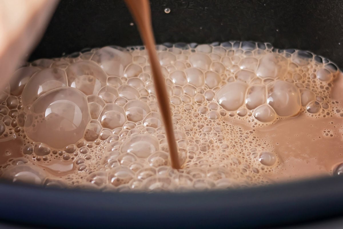 Chocolate milk being poured into crockpot.
