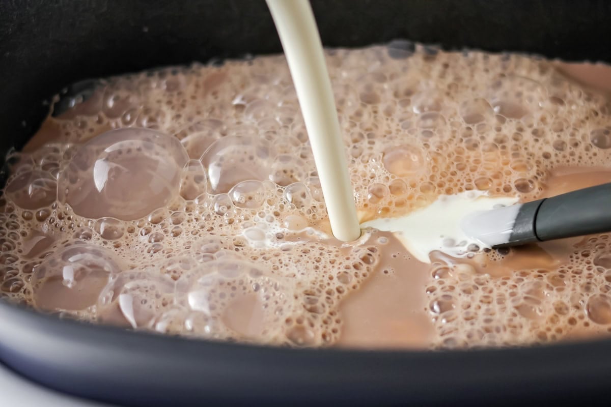Whipping cream being poured into slow cooker hot cocoa recipe.