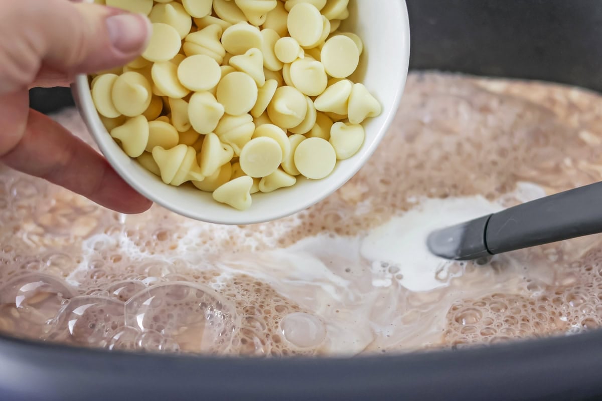 White chocolate chips being poured into crockpot hot chocolate recipe.