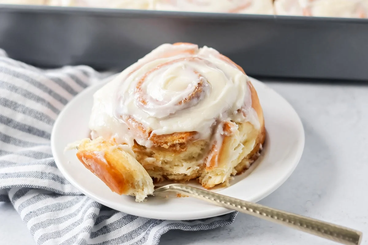 Easy cinnamon roll on white plate with bite taken out.