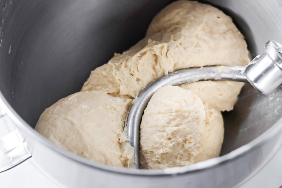 Cinnamon roll dough on dough hook in mixing bowl.