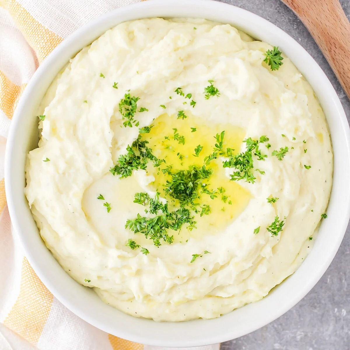 Close up image of make-ahead mashed potatoes recipe in white bowl with butter and parsley on top.